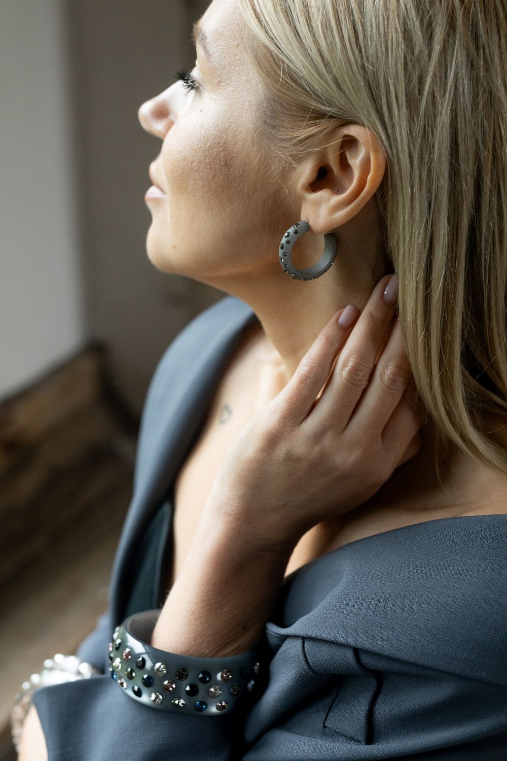 Frau mit breitem grauen Armreifen und Ohrringen mit Kristallen. Woman with large grey bangle and earrings with crystals.